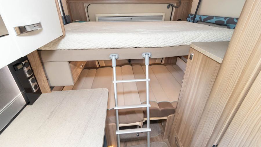 Interior de motorhome com cama elevada e escada retrátil em ambiente compacto e organizado