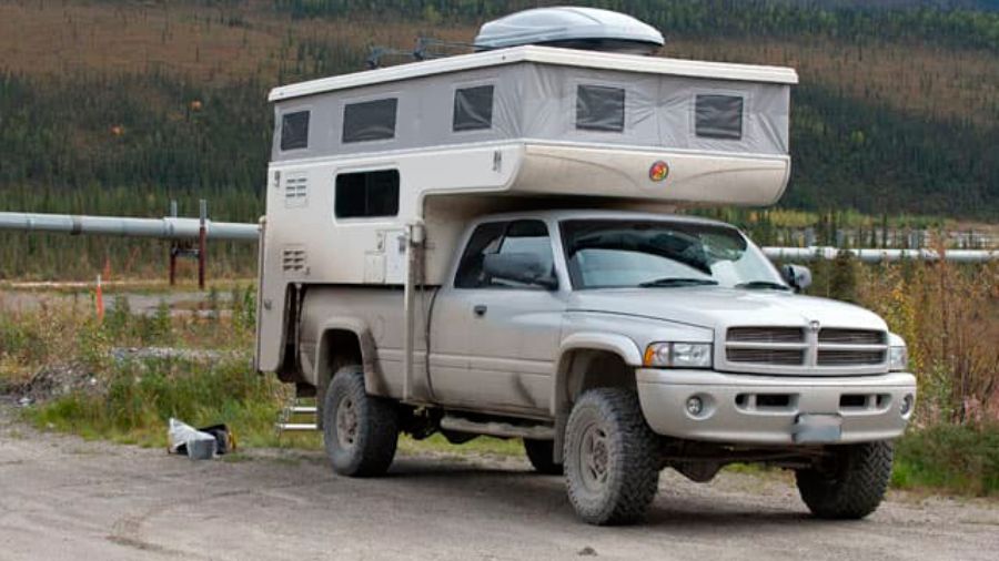 Camper acoplado a uma caminhonete 4x4 em estrada de terra na zona rural, usada como imagem ilustrativa no artigo