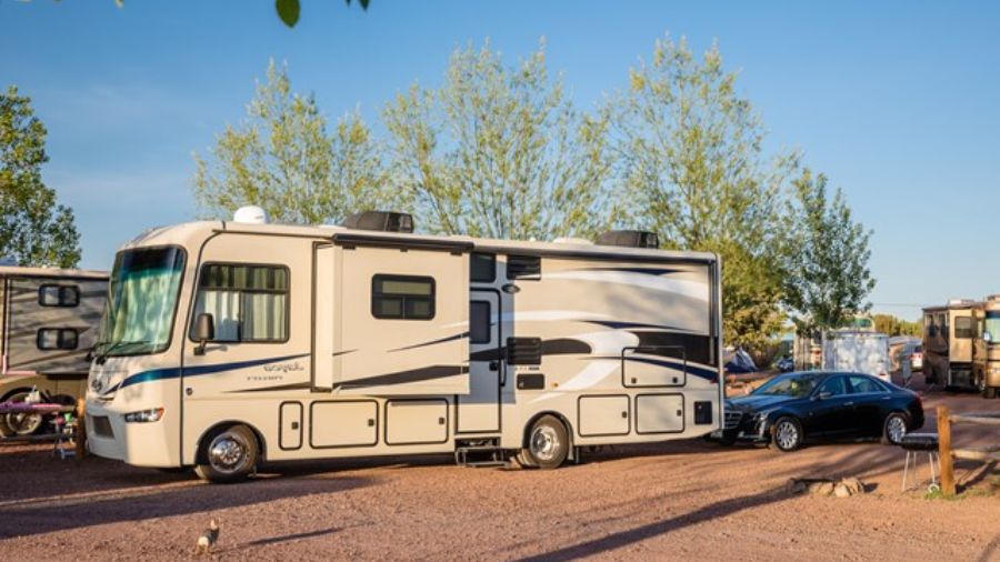 Motorhome estacionado em camping com carro ao lado durante o dia, ilustrando uma viagem de camping com conforto