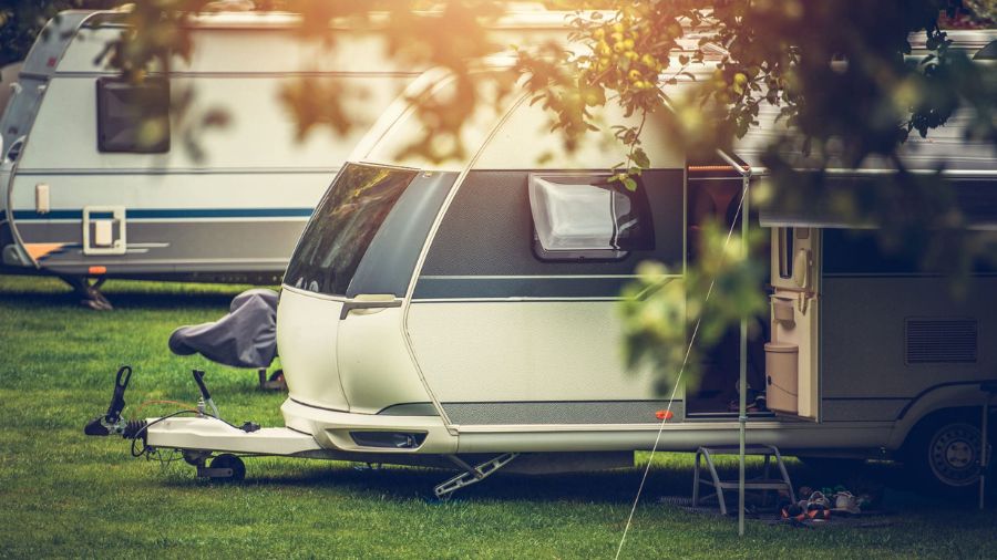 Trailer de camping montado em área gramada com sombra de árvores, representando um ambiente tranquilo ao ar livre
