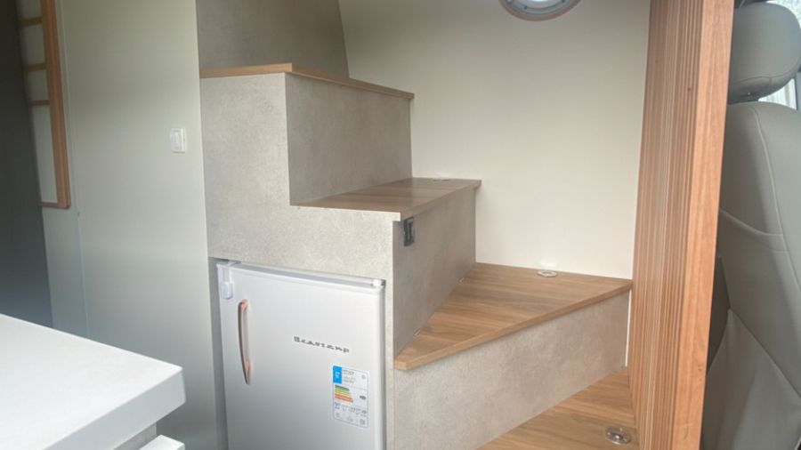 Escada de madeira e frigobar embutido no interior de um motorhome compacto